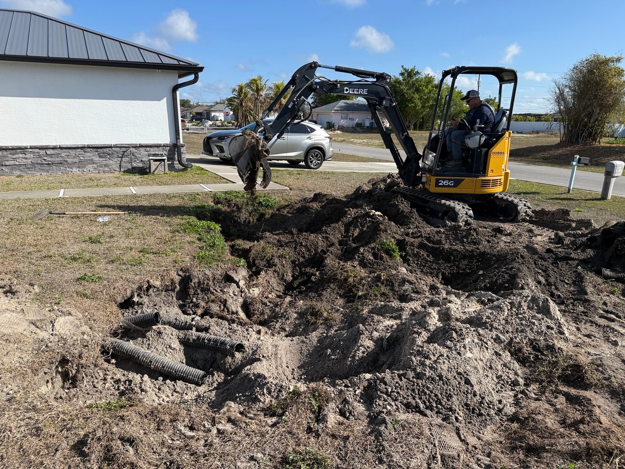 Mini excavator removing old septic tank drain field during septic abandonment — exposed leach field pipes
