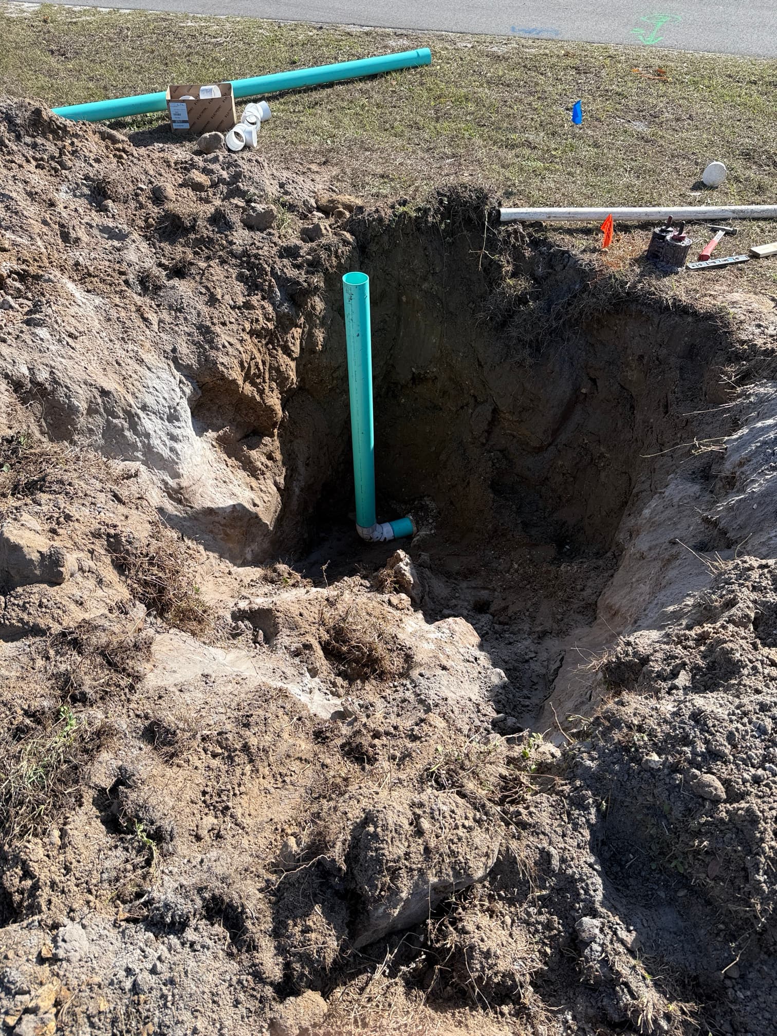 New sewer line cleanout and connection point installed in excavated trench — green PVC pipe with cleanout cap