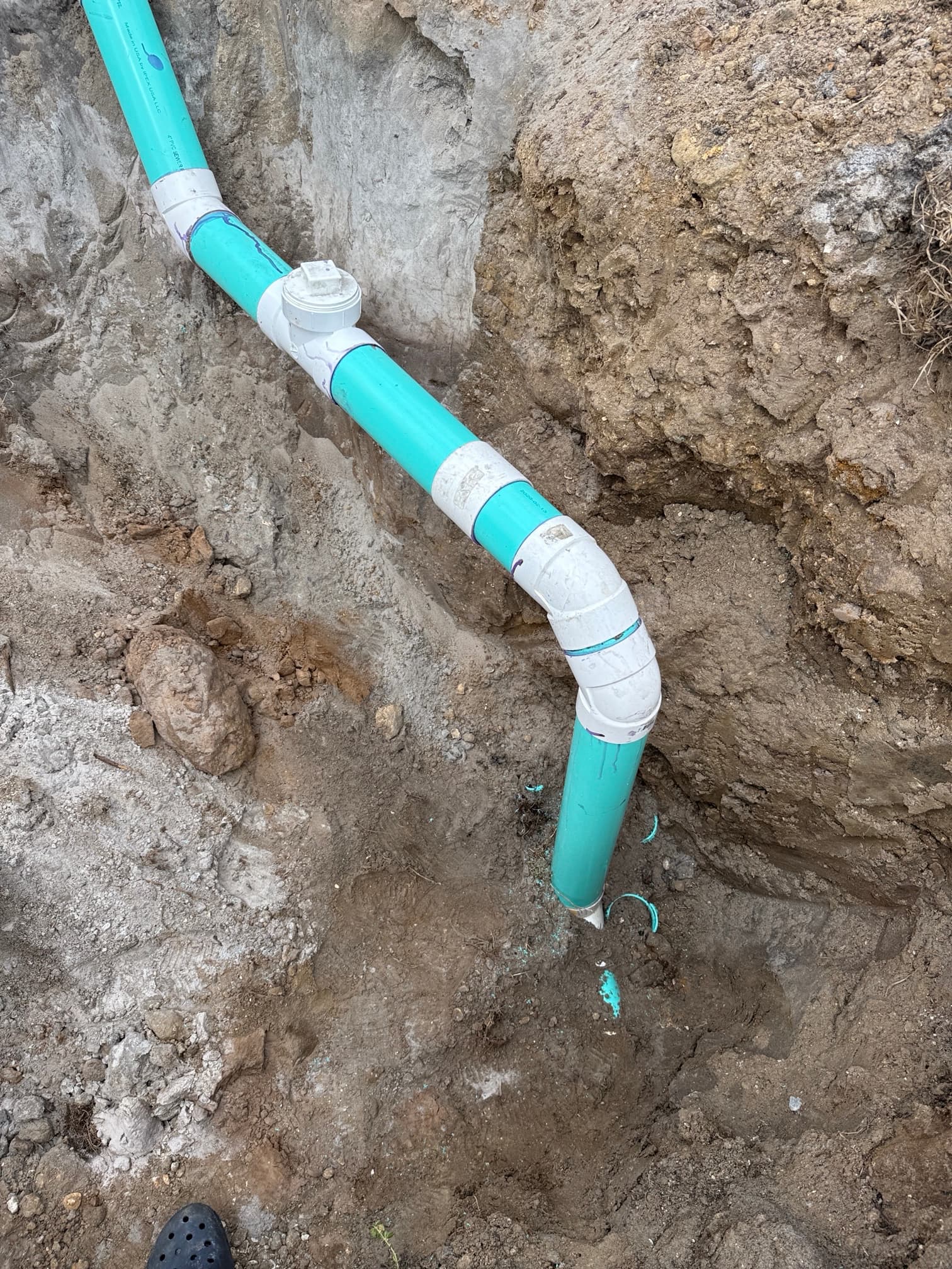 New green PVC sewer line with fittings and cleanout installed in trench — close-up of pipe connections