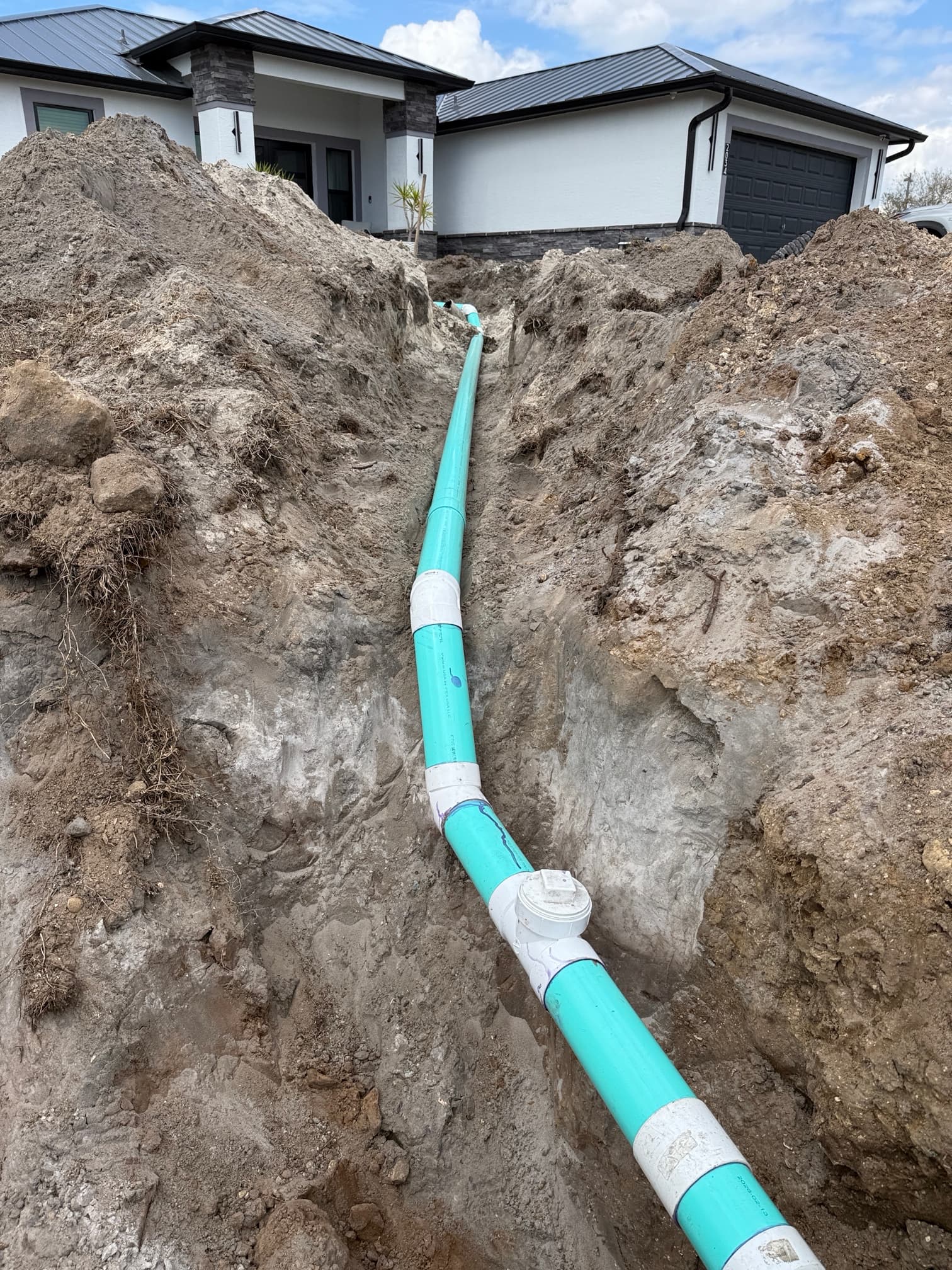 Sewer line running through deep trench from house to street — new PVC pipe with fittings ready for backfill