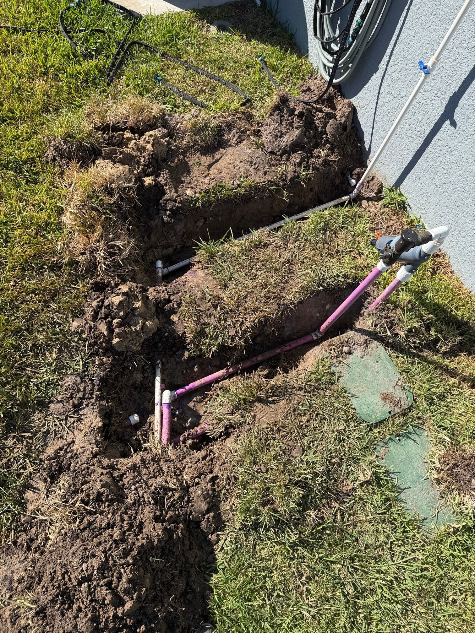 Irrigation and water service line trenching along house foundation — purple irrigation pipe and white water line